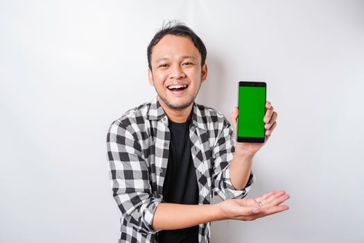 A portrait of a happy Asian man is smiling while showing copy space on his phone, isolated by white background photo
