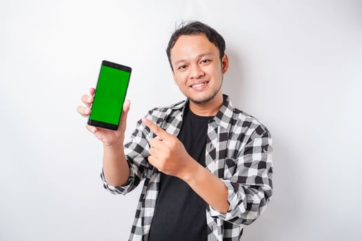 A portrait of a happy Asian man is smiling while showing copy space on his phone, isolated by white background photo