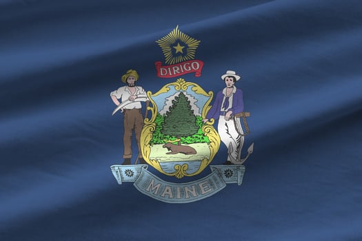 Maine US state flag with big folds waving close up under the studio light indoors. The official symbols and colors in banner photo