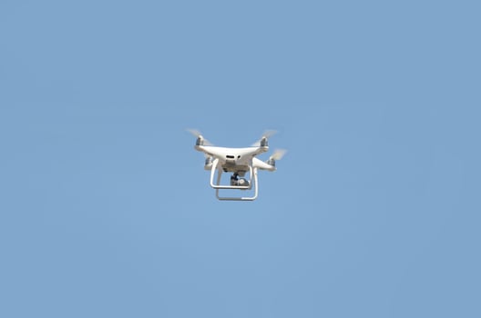 Big white drone hovering in a bright cloudless blue sky photo