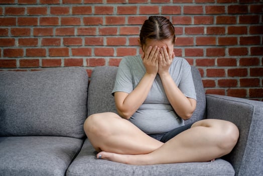 Stressed fat woman sitting on the sofa in the living room, feeling disappointed. She covered her face with her hands. photo