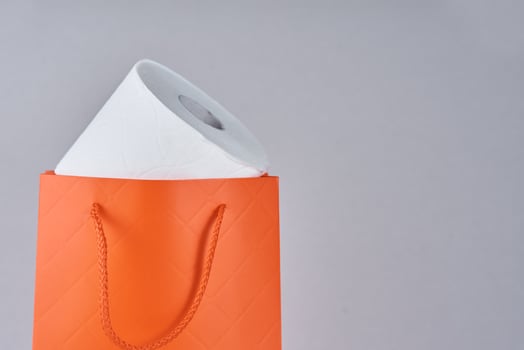 Toilet paper roll in shopping bag as gift on a gray background photo