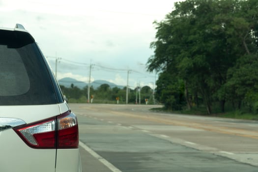 Rear side of white family car driving on the emptry road. Destination is a curved path lined with green trees and electric poles. photo