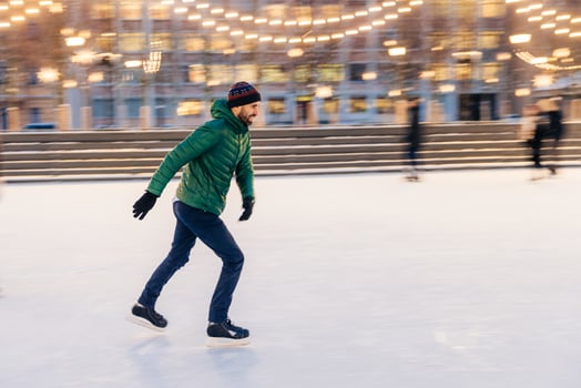 Middle aged male wears figure skates, being at ice rink in winter park, has fun with friend. Athlete speed skater demonstrates his talents on skating ring. Winter sport. Christmas vacations. photo