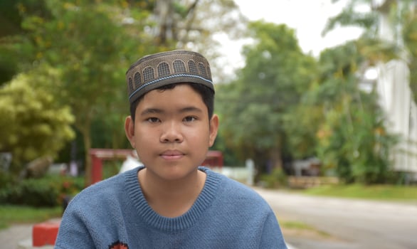 Portrait asian muslim or islamic boy sitting in the school park and smiling happily, soft and selective focus. photo