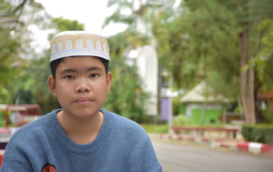 Portrait asian muslim or islamic boy sitting in the school park and smiling happily, soft and selective focus. photo