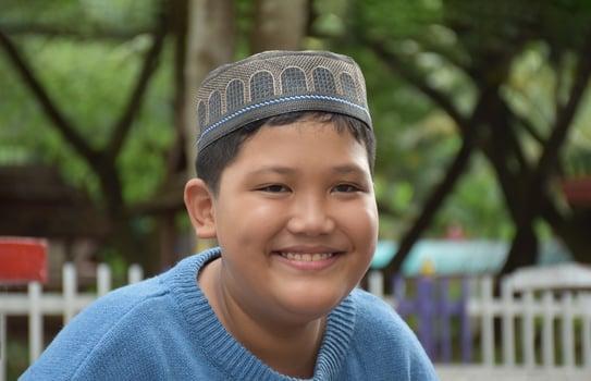 Portrait asian muslim or islamic boy sitting in the school park and smiling happily, soft and selective focus. photo