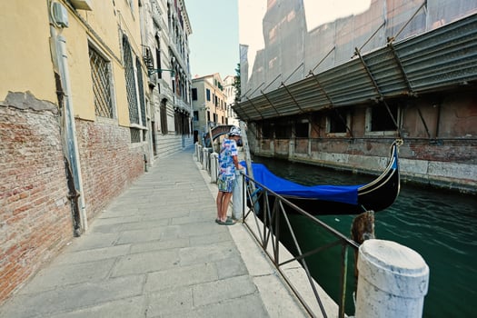 Boy stand near canal with covered gondola in Venice, Italy. photo