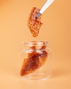 glass jar with brown cannabis wax, pieces of hardened resin of marijuana extract on an orange background photo