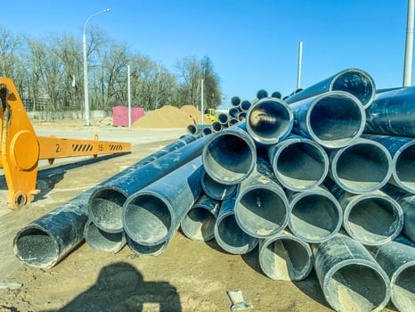 pipes for the construction of communications in the new microdistrict. black plastic pipes in sand and debris. yellow construction equipment next to the pipes photo