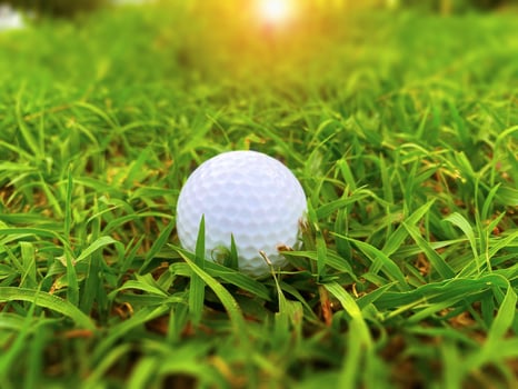 Golf ball close up on green grass on blurred beautiful landscape of golf course with sunrise,sunset time on background.Concept international sport that rely on precision skills for health relaxation. photo