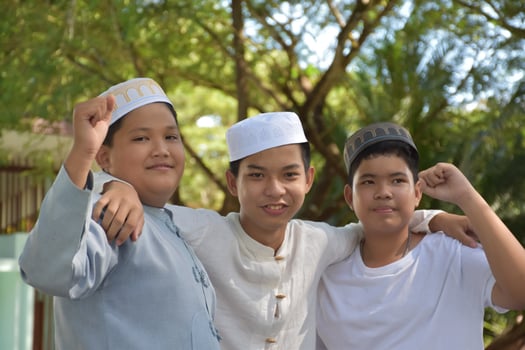 Young asian muslim boys raised hands, smilling and hugging each other to present happiness under the trees in the park, soft and selective focus. photo