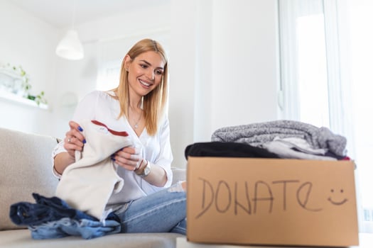 Young woman with donation box at home. Donation box for poor with clothing in female hands. Woman donates clothing to shelter. Cheerful woman holds box of donated clothing photo