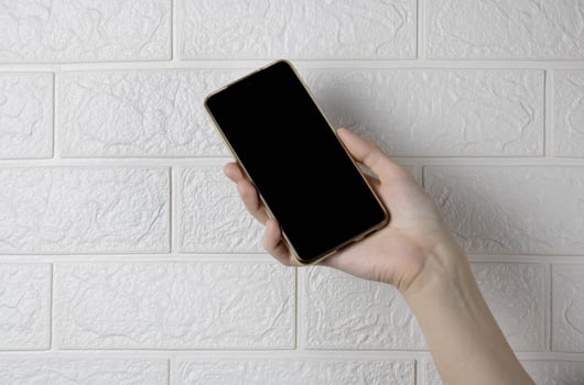 A hand holding a new smartphone on a white brick wall background photo