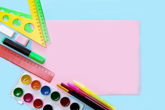 empty pink sheet on a blue background surrounded by school accessories - triangles, pens, watercolors, back to school concept, school background photo