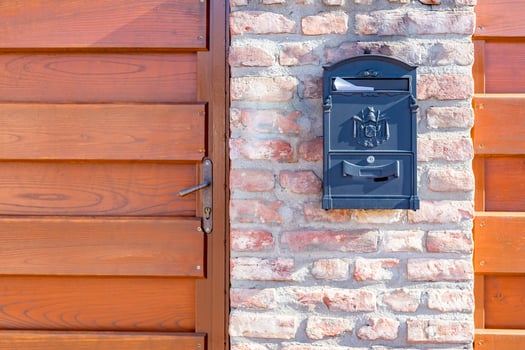 Old steel, iron mail box on stone brick wall, next to wooden fence on building or house door. Home related object, mail box photo