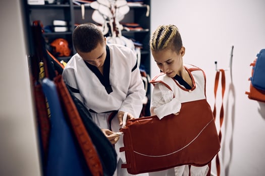 Disabled taekwondo fighter dressing up chest body armor with help of her coach in locker room. photo