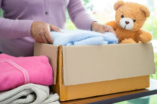 Holding clothing donation box with used clothes and doll at home to support help for poor people in the world. photo