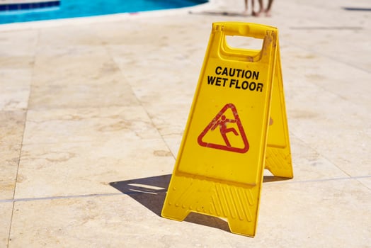 Yellow wet floor caution sign in summer day, closeup photo