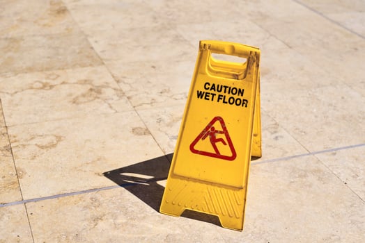 Yellow wet floor caution sign in summer day, closeup photo