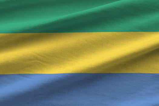 Gabon flag with big folds waving close up under the studio light indoors. The official symbols and colors in banner photo