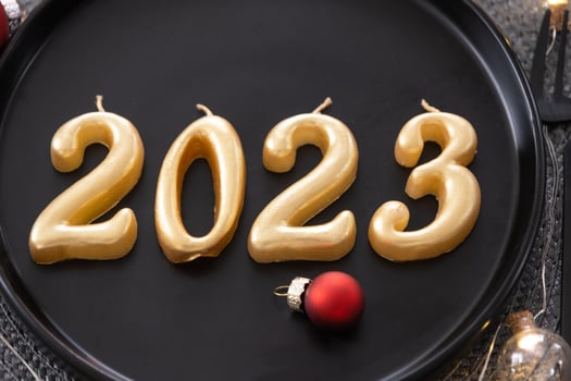 Golden figures 2023 from candles on a black plate on a festive table with a New Year's serving. Loft-style interior, party, feast. Wicker napkin, fork, knife photo
