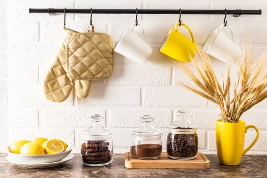 front view of the kitchen marble countertop with cans of coffee and a bowl of lemons. kitchen rail with mugs on a white brick wall. photo