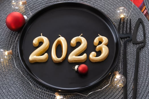 Golden figures 2023 from candles on a black plate on a festive table with a New Year's serving. Loft-style interior, party, feast. Wicker napkin, fork, knife photo