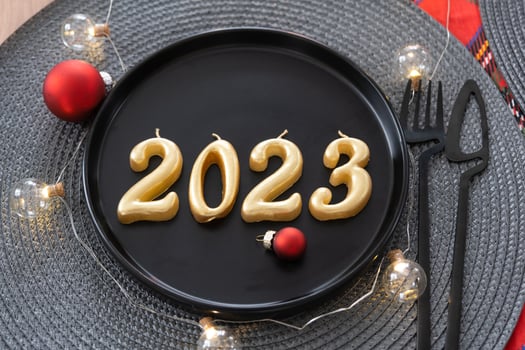Golden figures 2023 from candles on a black plate on a festive table with a New Year's serving. Loft-style interior, party, feast. Wicker napkin, fork, knife photo