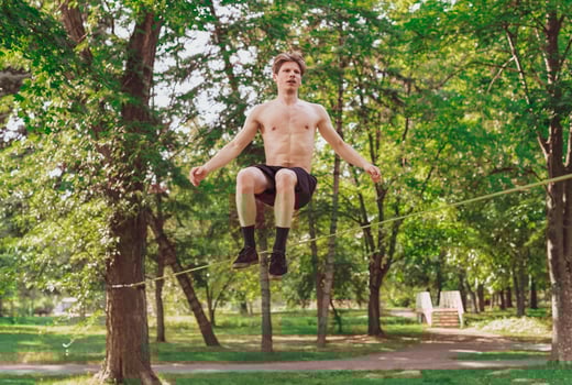 Young man balancing and jumping on slackline. Man walking, jumping and balancing on rope in park. photo