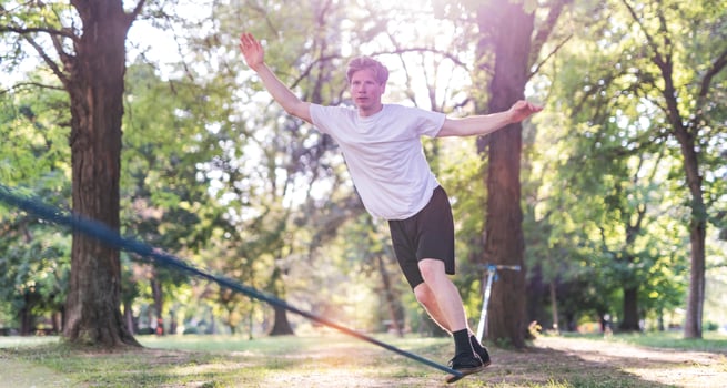 Young man balancing and jumping on slackline. Man walking, jumping and balancing on rope in park. photo
