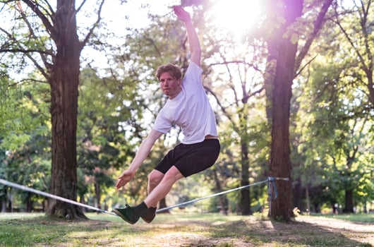 Young man balancing and jumping on slackline. Man walking, jumping and balancing on rope in park. photo