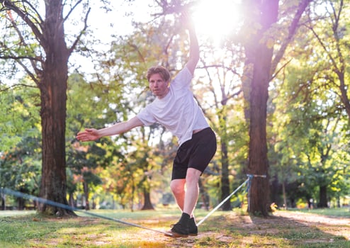 Young man balancing and jumping on slackline. Man walking, jumping and balancing on rope in park. photo