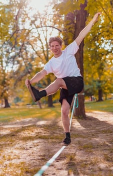 Young man balancing and jumping on slackline. Man walking, jumping and balancing on rope in park. photo