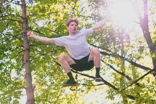 Young man balancing and jumping on slackline. Man walking, jumping and balancing on rope in park. photo