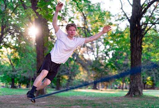 Young man balancing and jumping on slackline. Man walking, jumping and balancing on rope in park. photo