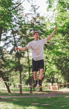 Young man balancing and jumping on slackline. Man walking, jumping and balancing on rope in park. photo