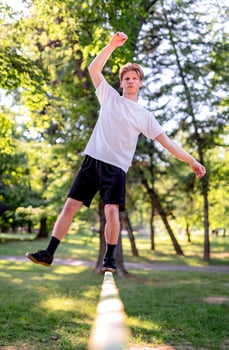 Young man balancing and jumping on slackline. Man walking, jumping and balancing on rope in park. photo