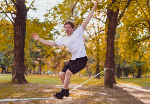 Young man balancing and jumping on slackline. Man walking, jumping and balancing on rope in park. photo