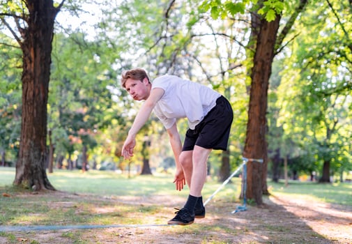 Young man balancing and jumping on slackline. Man walking, jumping and balancing on rope in park. photo