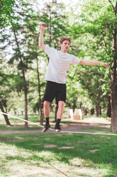 Young man balancing and jumping on slackline. Man walking, jumping and balancing on rope in park. photo
