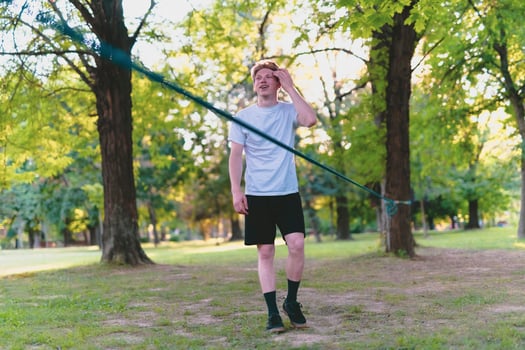 Young man balancing and jumping on slackline. Man walking, jumping and balancing on rope in park. photo