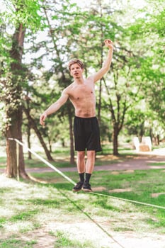 Young man balancing and jumping on slackline. Man walking, jumping and balancing on rope in park. photo