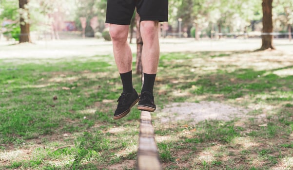 Young man balancing and jumping on slackline. Man walking, jumping and balancing on rope in park. photo