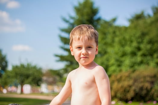 A cute blond boy experiences the joy of walking on a summer day by the river, sitting on the juicy grass. Funny facial expression. summer heat, a child without a T-shirt. photo