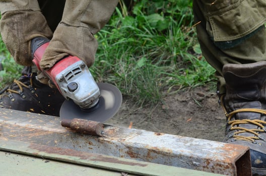 Electric wheel grinding on steel structure outdoors. Old manual worker in protective gloves cutting metal door with grinder photo