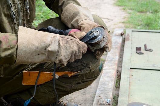 Electric wheel grinding on steel structure outdoors. Old manual worker in protective gloves cutting metal door with grinder photo