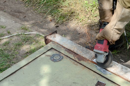Electric wheel grinding on steel structure outdoors. Old manual worker in protective gloves cutting metal door with grinder photo