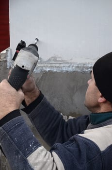 An elderly workman drills a hole in a styrofoam wall for the subsequent installation of a plastic reinforcing dowel. Creating holes in the wall with a drill. Warming of the building facade photo