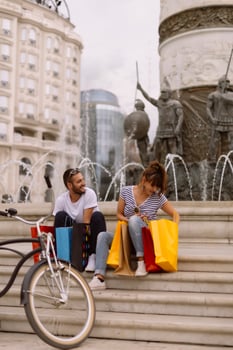 Portrait of cheerful Caucasian young couple man and woman holding many paper bags after shopping while walking and talking on street. Happy family couple with packages outdoor. Buying concept photo